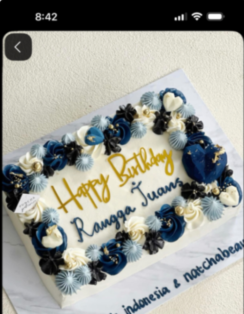 A rectangular white soft-icing cake with a border of navy blue, light blue, and white icing rosettes, gold dragees, and blue heart-shaped chocolates.
