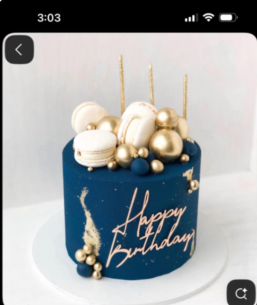 Navy blue birthday cake with gold spheres, white macarons, and a rose gold Happy Birthday topper.