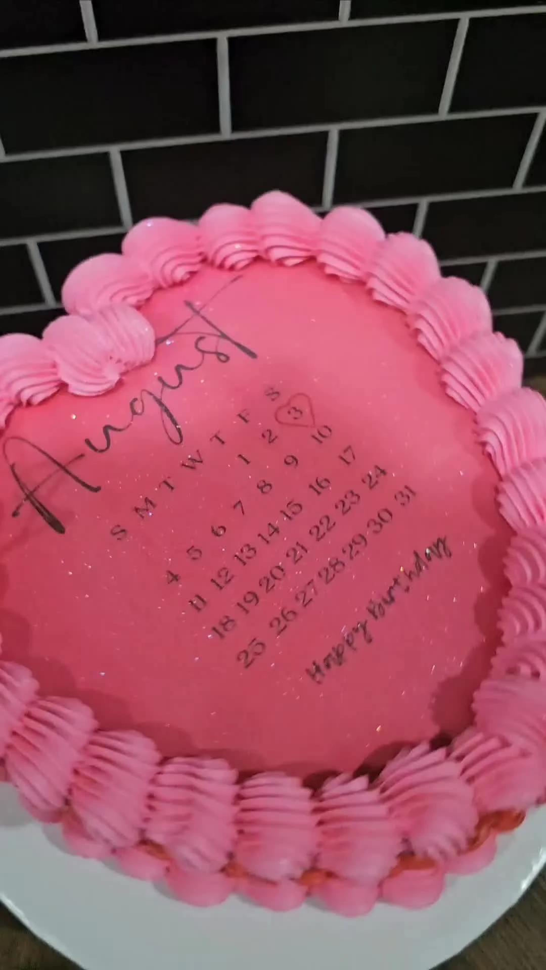Heart-shaped pink minimalist cake with a black August calendar design and piped pink icing borders.