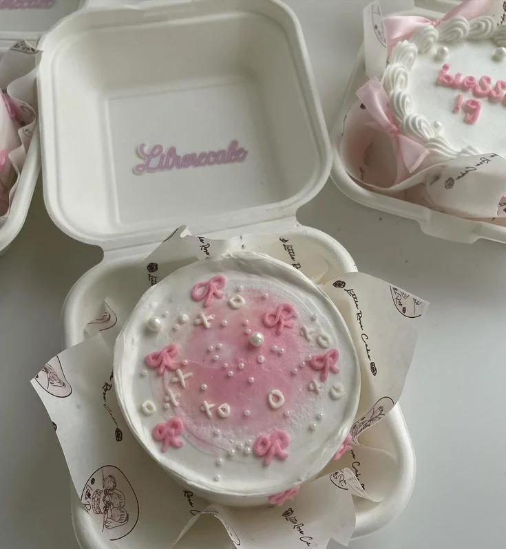 White bento cake with pink watercolor center, pink and white icing bows, and white pearl sprinkles in a clamshell box.