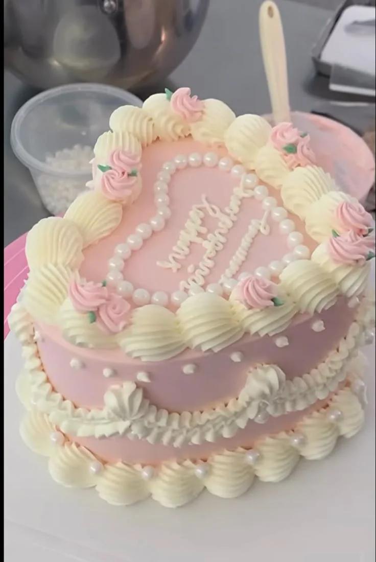Heart-shaped pink vintage cake with white piped ruffles, pink icing roses, and edible pearl heart border.