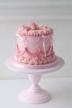 Elegant pink vintage-style cake with intricate piped ruffles, swags, and pink macarons on a matching pink cake stand.