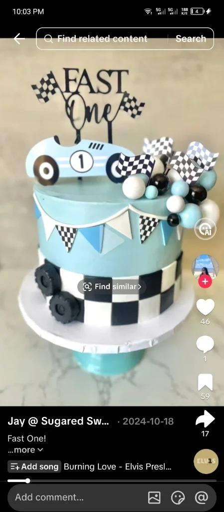 Light blue racing themed cake with a checkered pattern, racing car topper, and checkered flags for a first birthday celebration.