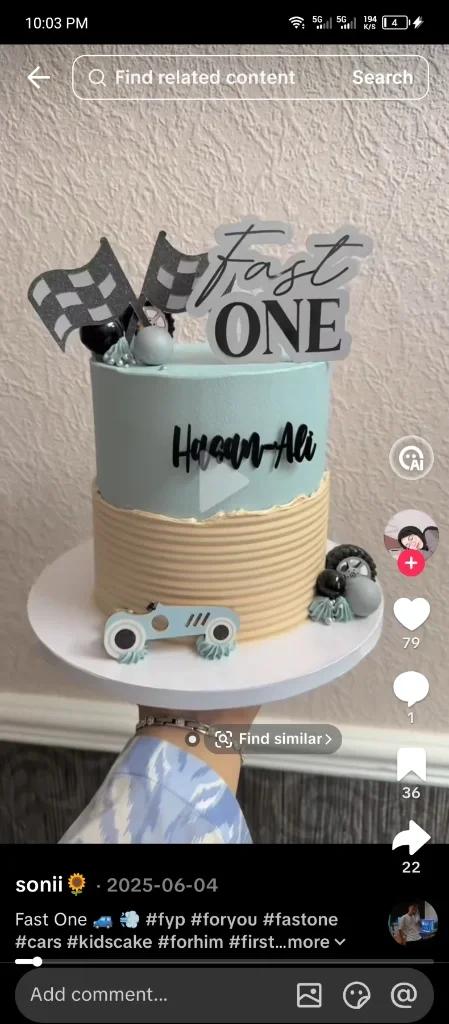 A two-toned light blue and tan textured cake with a racing car theme, featuring checkered flags and a 'Fast One' topper.