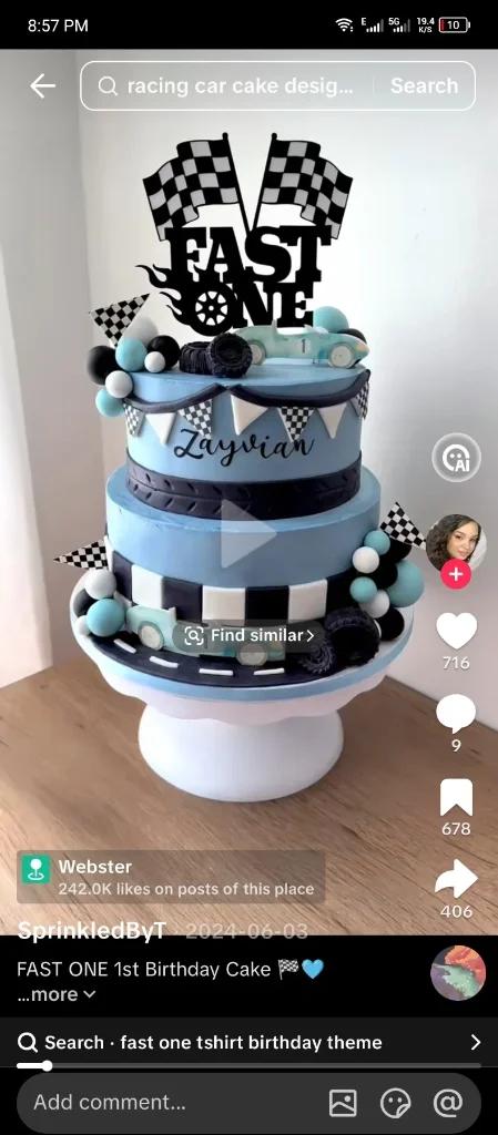 Two-tier light blue racing car themed birthday cake with checkered flags, fondant tires, and a 'Fast One' topper.