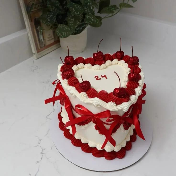 Heart-shaped white cake with red icing ruffles, red glitter cherries, and red satin bows for a 24th birthday celebration.