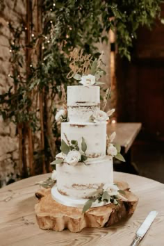 Three-tier semi-naked rustic wedding cake decorated with fresh white roses and green leaves on a wooden base.