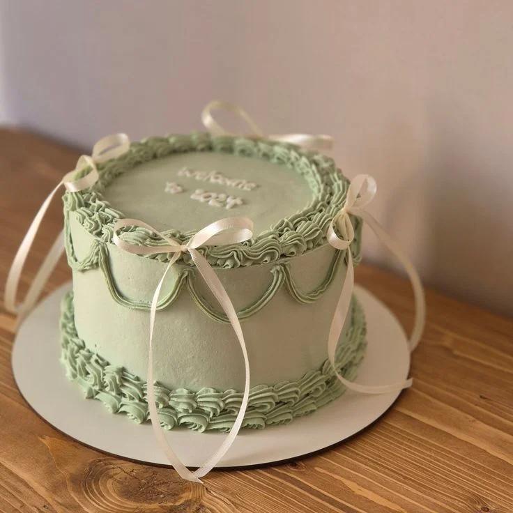 Sage green minimalist cake with piped ruffles, draped icing swags, and delicate white satin ribbons.