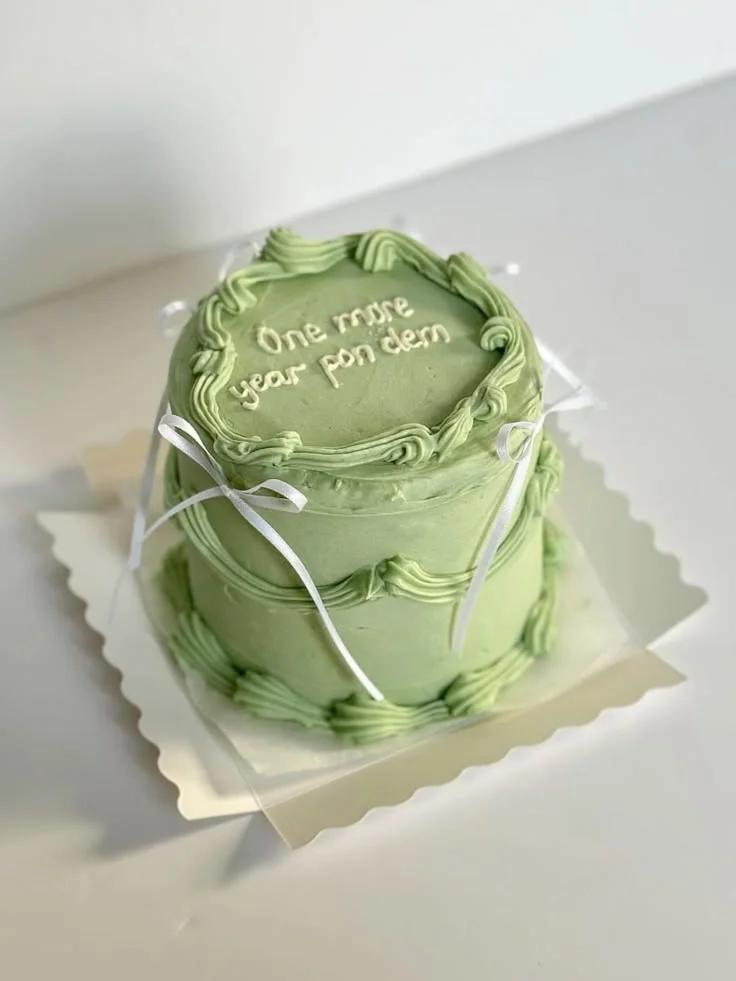 Minimalist sage green cake with piped borders, white satin ribbons, and a handwritten message on top.
