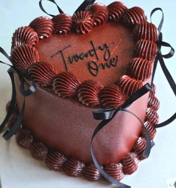 Heart-shaped chocolate cake with dark red piped icing borders, black ribbons, and a 'Twenty One' topper.