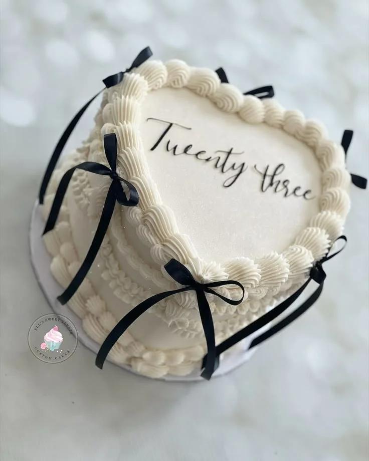 Heart-shaped white vintage lambeth cake with black satin bows and 'Twenty three' piped icing text.