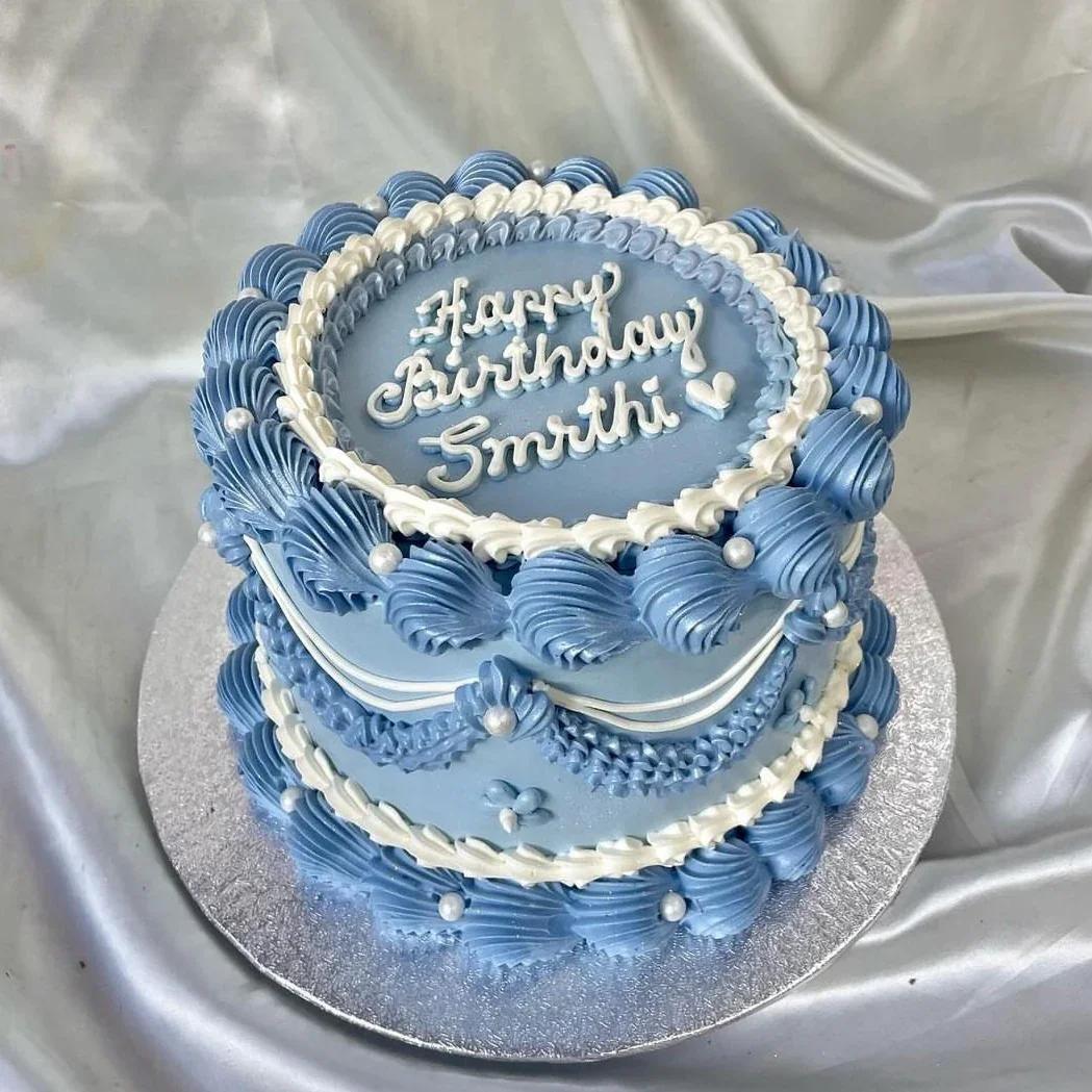 Elegant light blue vintage-style cake with intricate white and blue piped icing ruffles, swags, and pearl accents.