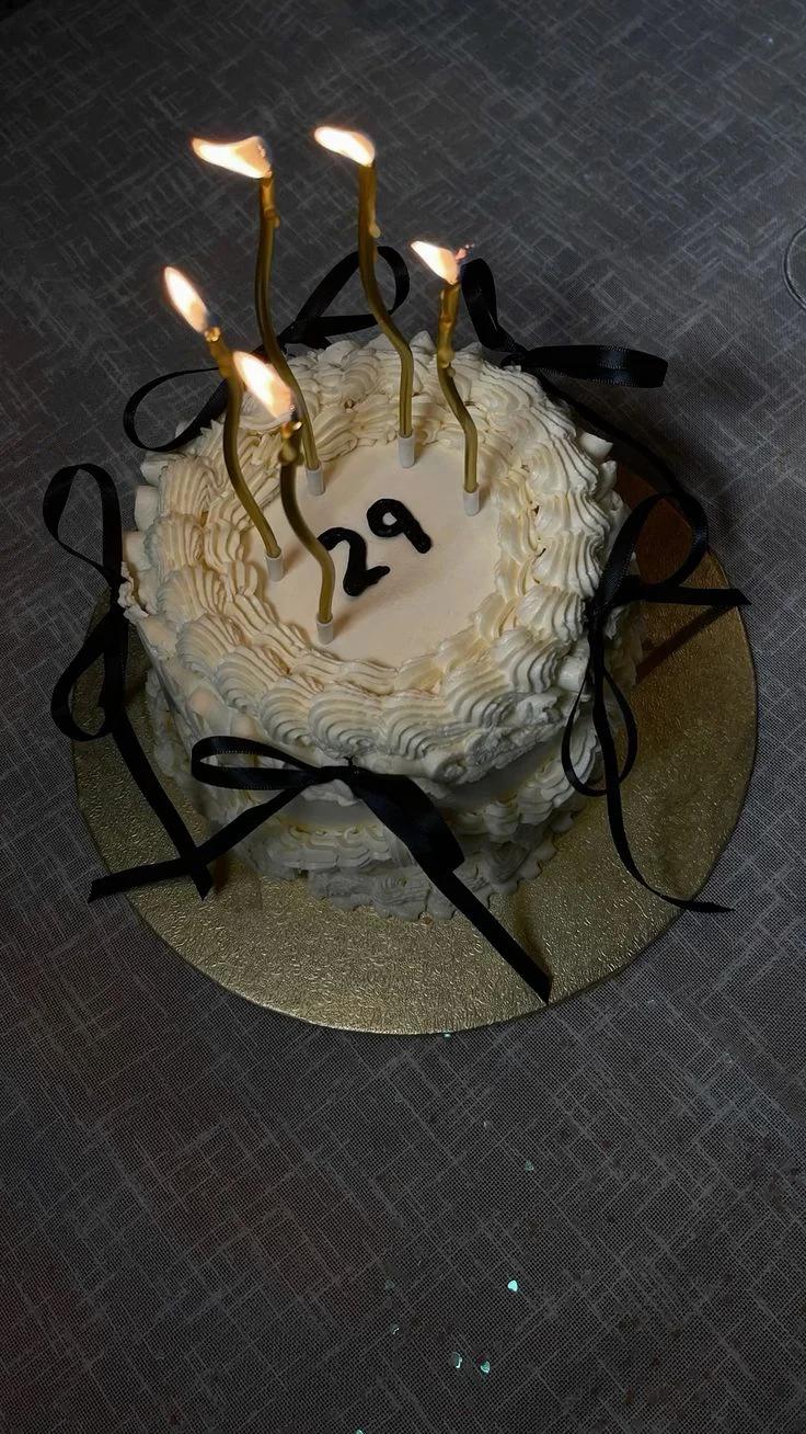 White vintage-style heart cake with ruffled icing, black satin bows, and gold taper candles for a 29th birthday.