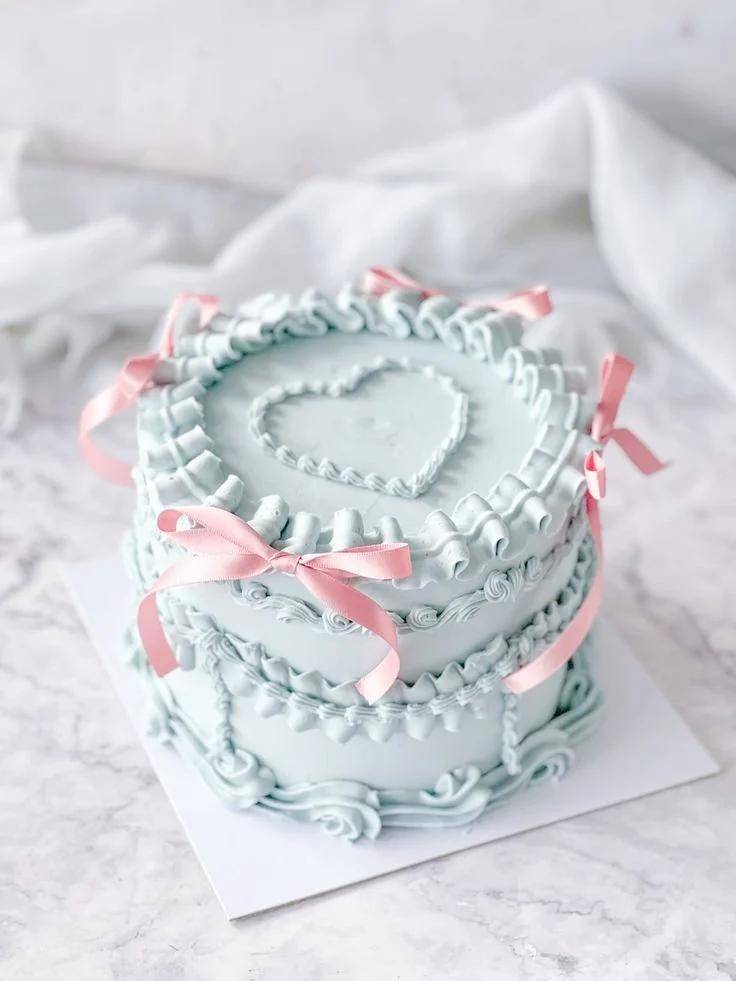 Light blue vintage heart cake with intricate ruffles, pink satin bows, and a piped icing heart on top.
