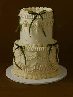 Elegant 2-tier ivory vintage-style cake with intricate piped ruffles, swags, and dark green satin ribbons.