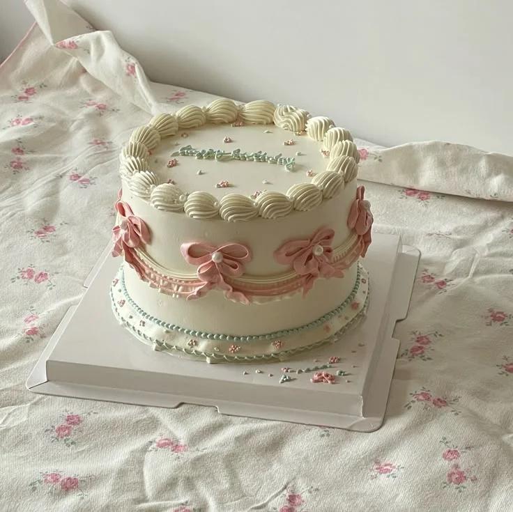 Elegant white vintage-style cake with pink piped bows, ruffles, and a light blue Happy Birthday message.