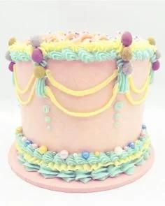 Tall pink vintage-style cake with pastel blue and yellow piped ruffles, draped icing swags, and colorful edible pearls.