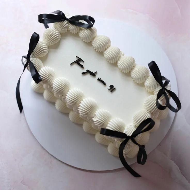 Elegant white rectangular cake with thick piped cream borders and black satin bows, featuring a minimalist black message in the center.