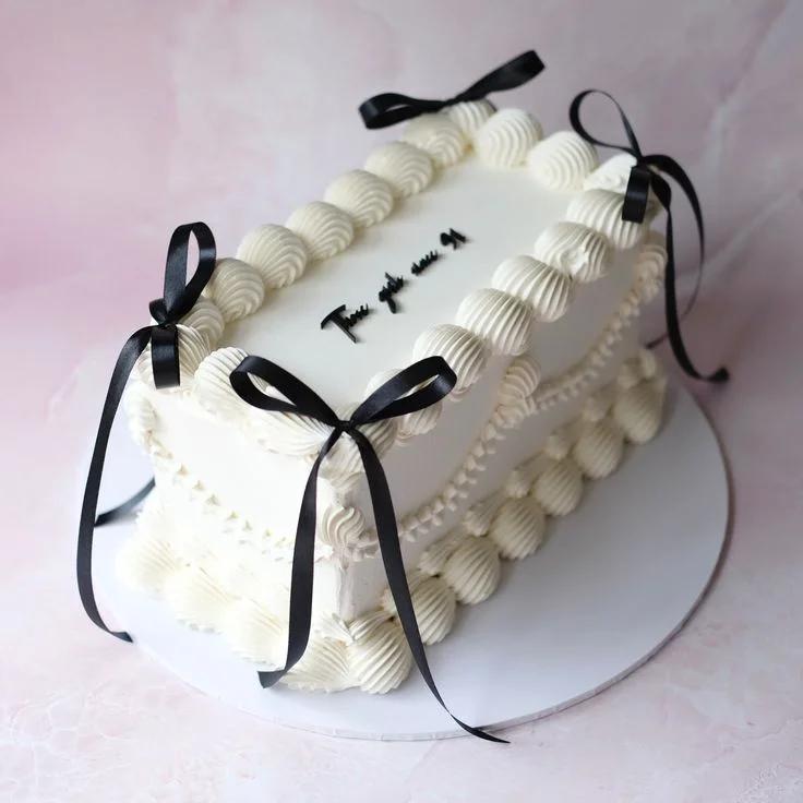 Elegant white rectangular cake with piped cream borders, black satin ribbons, and a minimalist black message on top.