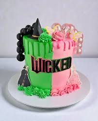 A split-design Wicked musical themed cake with green and pink icing, a witch hat, bubbles, and a 'Wicked' logo.